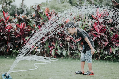 a kid getting splashes by a water hose